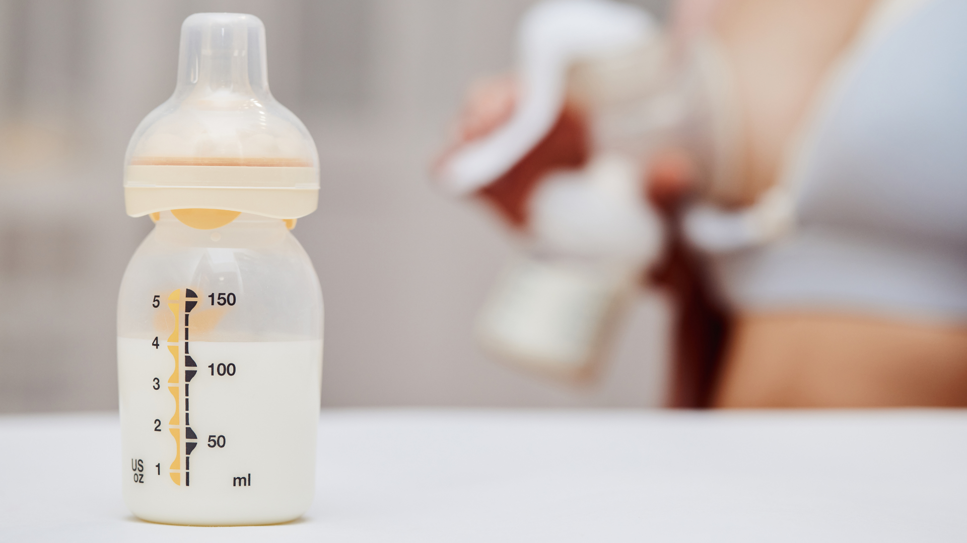 Medela baby bottle will breastmilk and mom pumping in the background