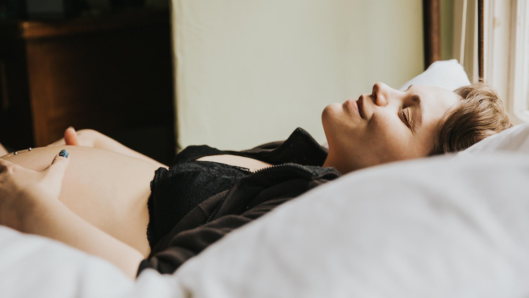 Woman laying down and smiling in labor while resting her hands on her pregnant belly